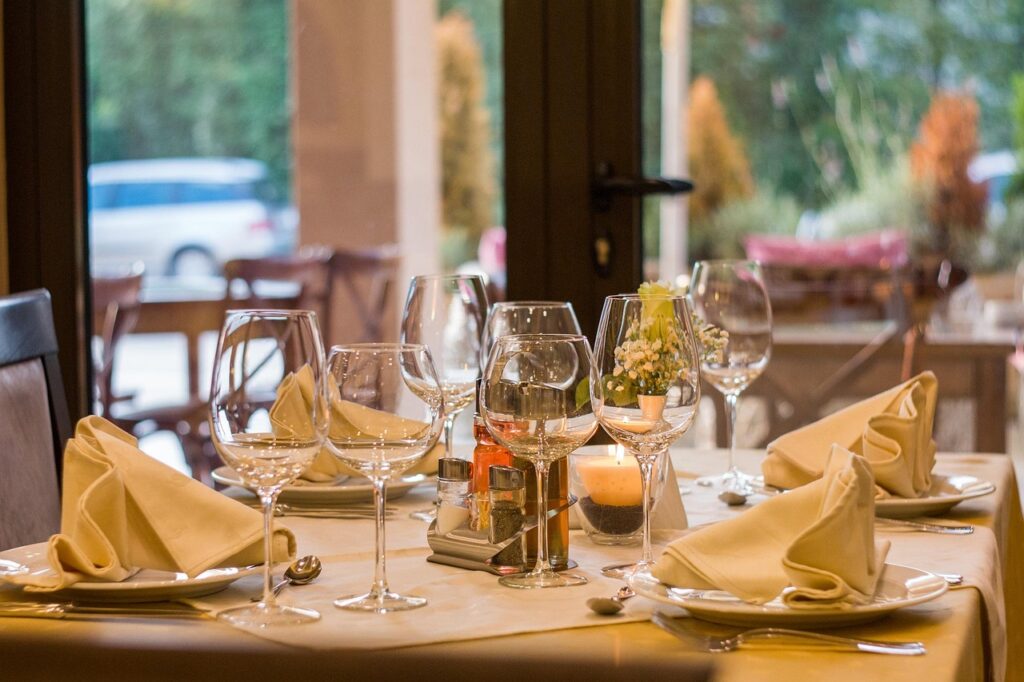 dining table in a restaurant set with cutlery, plates, wine glasses and napkins
